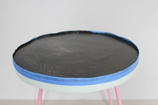 A round stool has a black top and pink legs.
