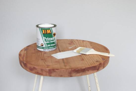 A can of primer and a paintbrush sit on a round chair.