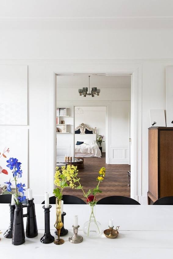 Blue and green flowers sit on a kitchen counter that looks out into the living room where a door opens into a bedroom where the bed can be seen.
