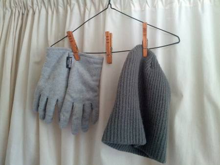 Gloves and a beanie hanging from clothespins on a hanger.