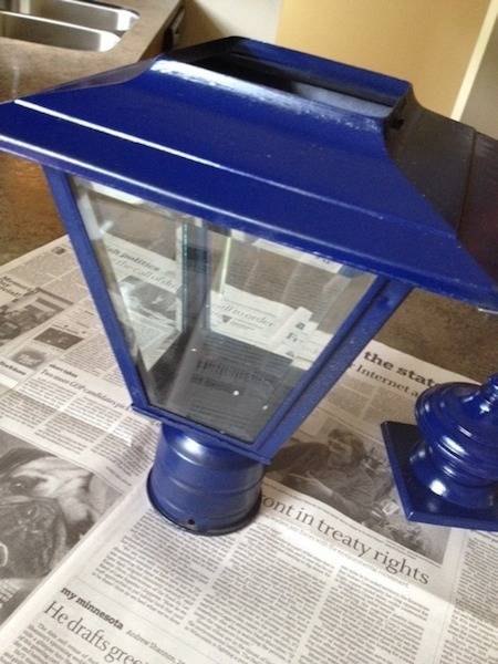 A bright blue freshly painted  porch lantern sits on newspaper.