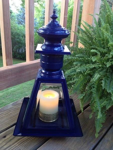 A dark blue shiny pagoda tea candle holder on a wooden deck next to a fern plant.