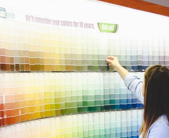 A dark haired woman choosing a paint color card among three rows of paint color cards.