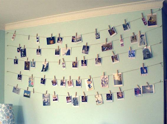 A wall has a bunch of photos hanging from strings on it.