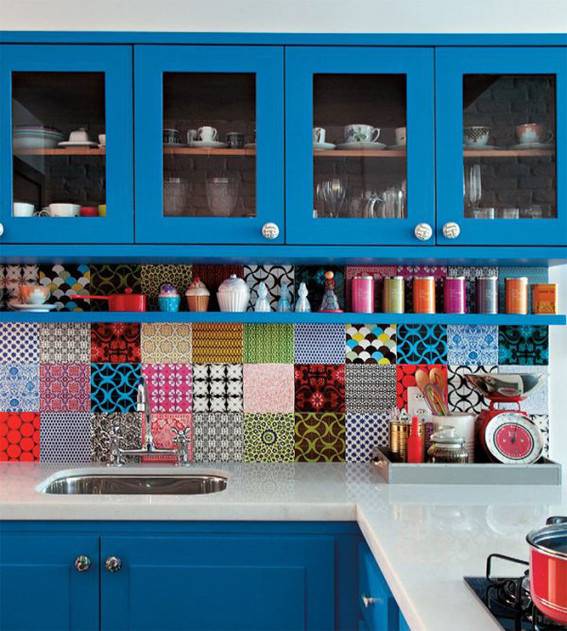 A blue kitchen has colorful patches of backsplash on the wall.