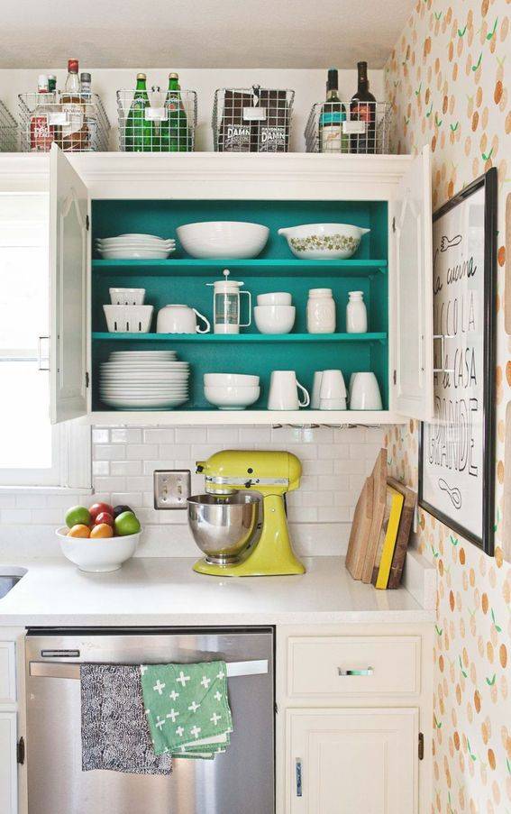 A kitchen has a white desk and teal cupboard.