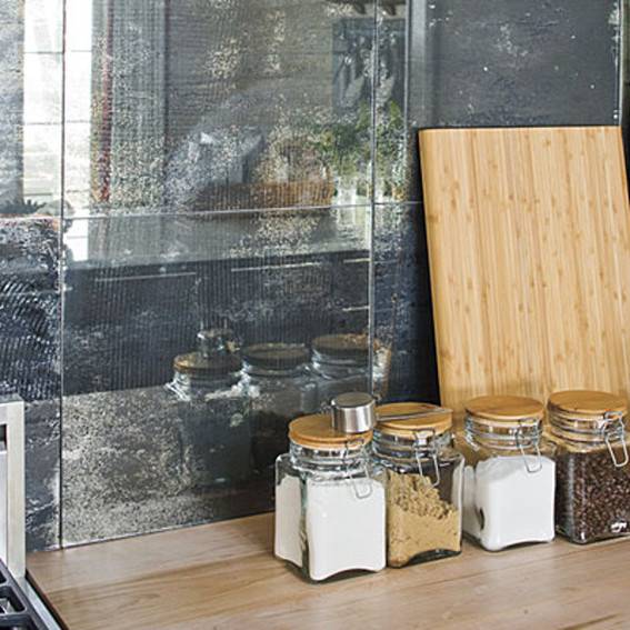 Wood cutting board and row of square glass spice jars in front of shiny black marble-look tiles.