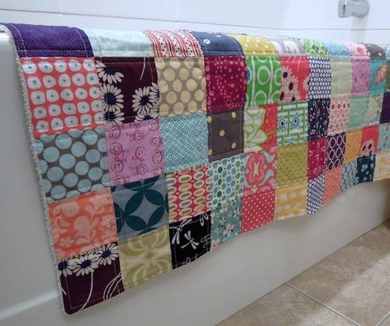 A multicolored quilt laying on the edge of a bathtub.