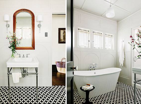 A modern bathroom has classic touches like black and white floors, a modern claw foot type of tub, and 1930s style sink.