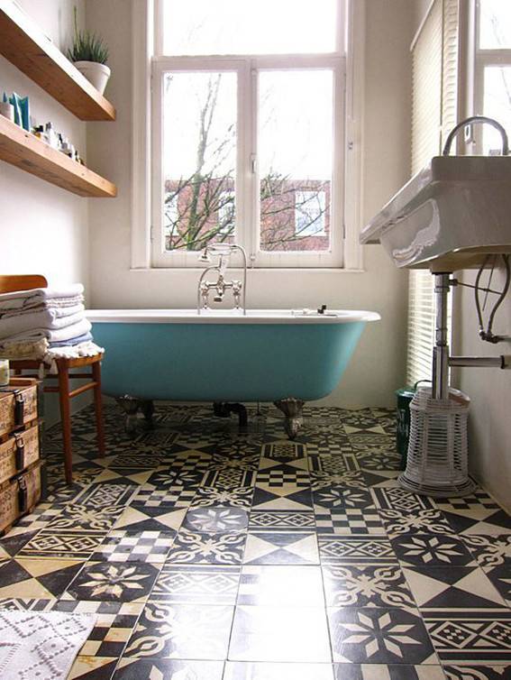 Mismatched black tan and white decorative tile line the floor of a bathroom with a teal clawfoot bathtub.