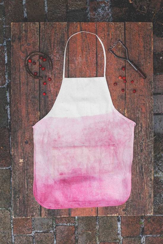 Apron dyed in a reddish pink dye on top of a wood table.