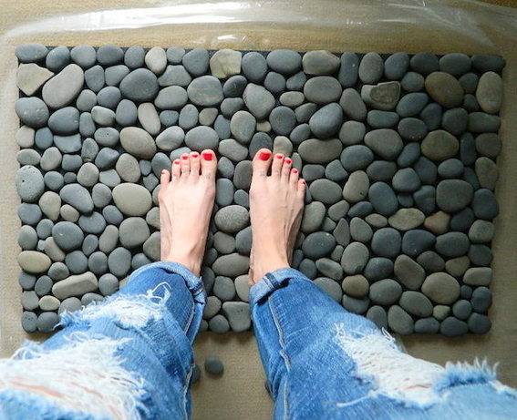 A woman's legs and feet with red nailpolish are standing on flattened round rocks.
