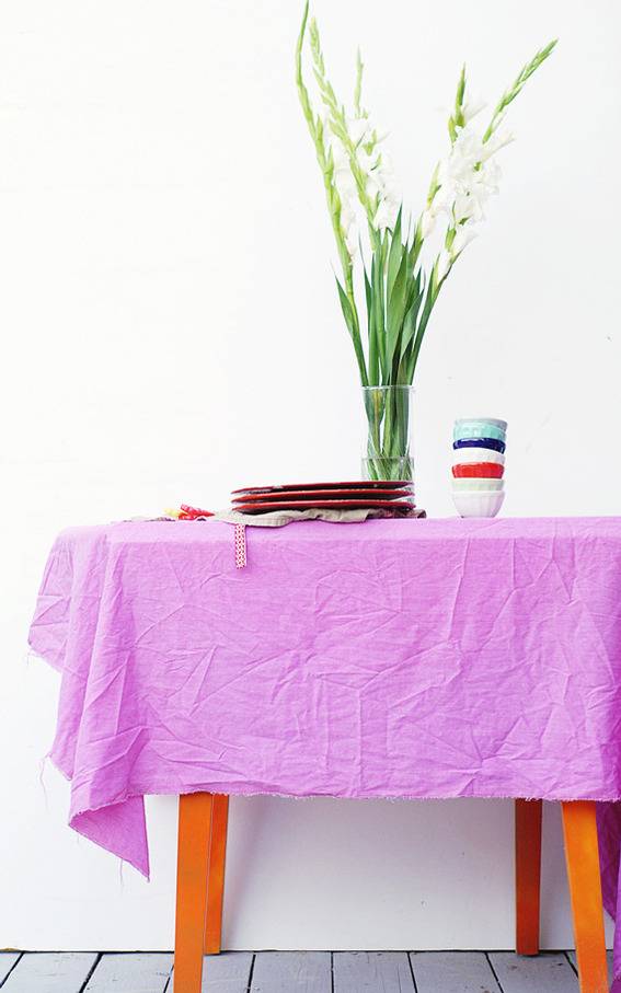 A bright green plant sits on a purple chiffon hung over an orange table to be the tablecloth.