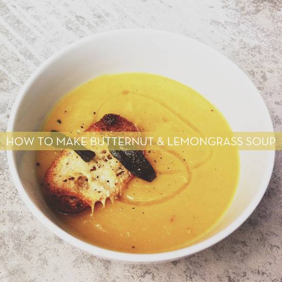 A crusty piece of bread sits in a large white bowl of butternut squash soup.