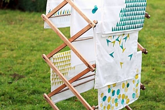 A wooden blanket rack with pieces of white and green cloth hanging on them.