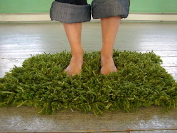 A person standing in a bathmat made of shrubbery/plants.