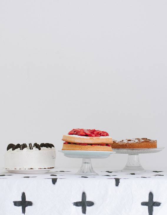 A trio of cakes atop a table with a black and white tablecloth.