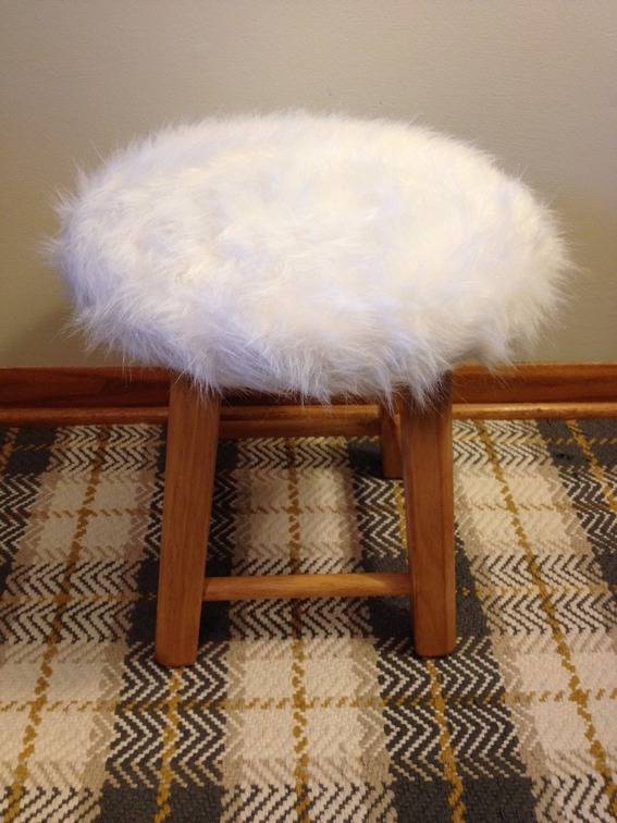 A fuzzy white stool with brown legs.
