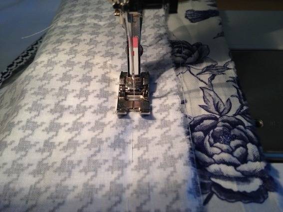 Houndstooth fabric is folded underneath presser foot of a sewing machine.