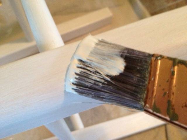 A brush has white paint on it by the surface it is painting.