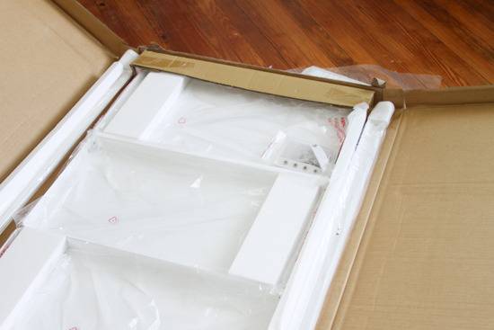 A long rectangular cardboard box is open and shows white components.