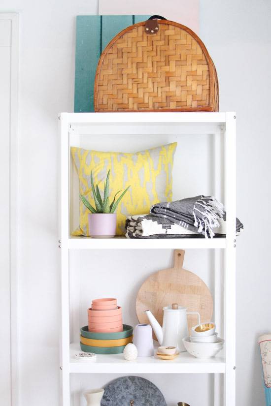 White shelf consisting of a basket, plants, pillow, and other various knick-knacks.