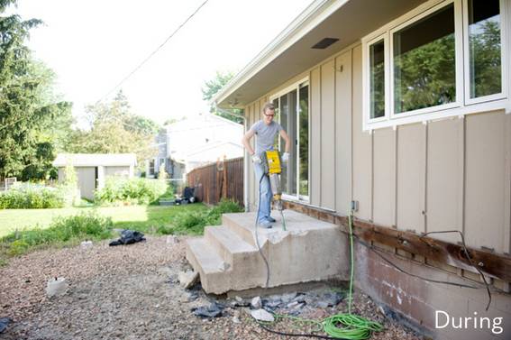 A person poses with a tool on concrete porch steps by a trailer.