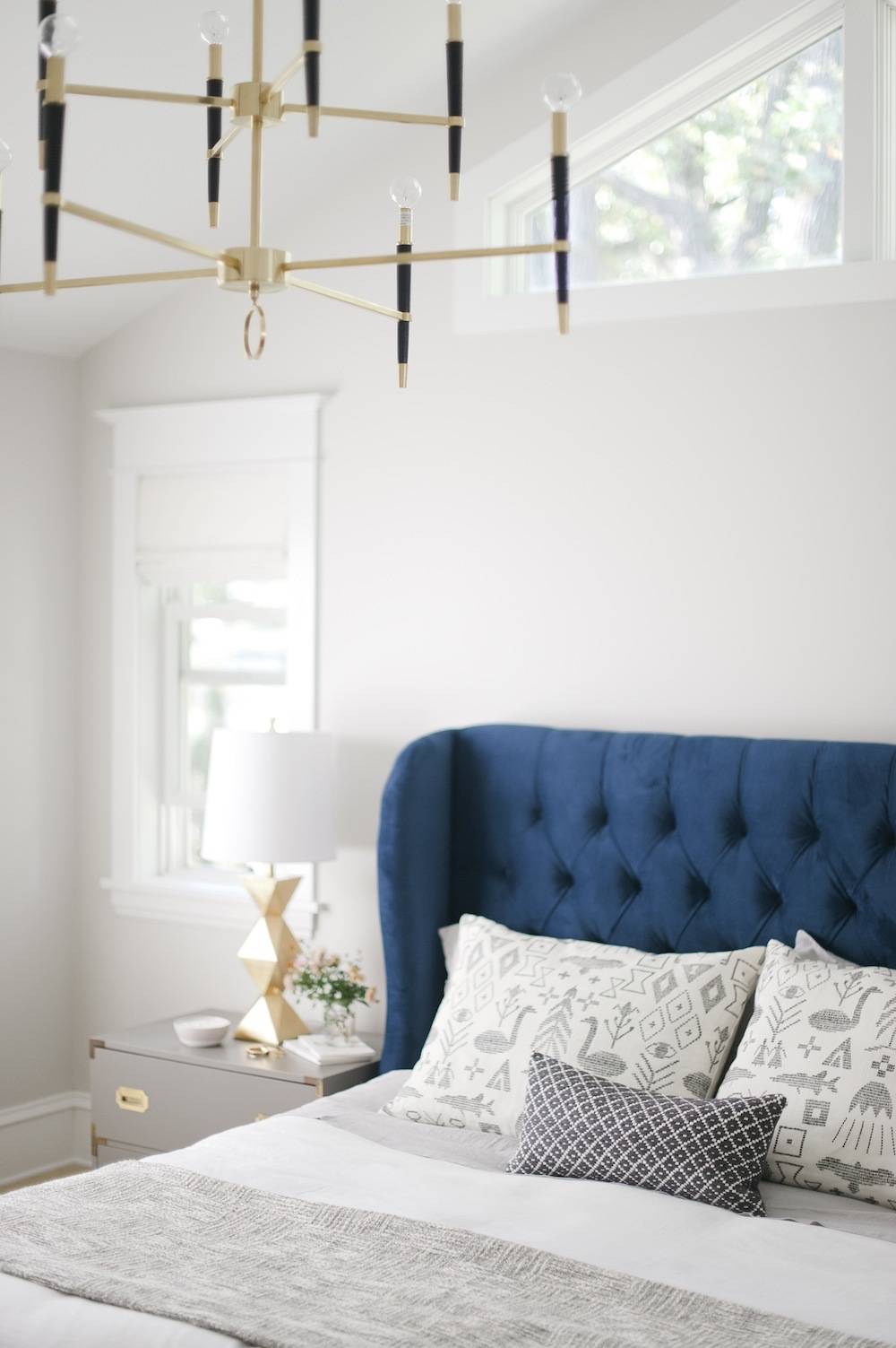 A bed with a blue material headboard sits in a white bedroom.