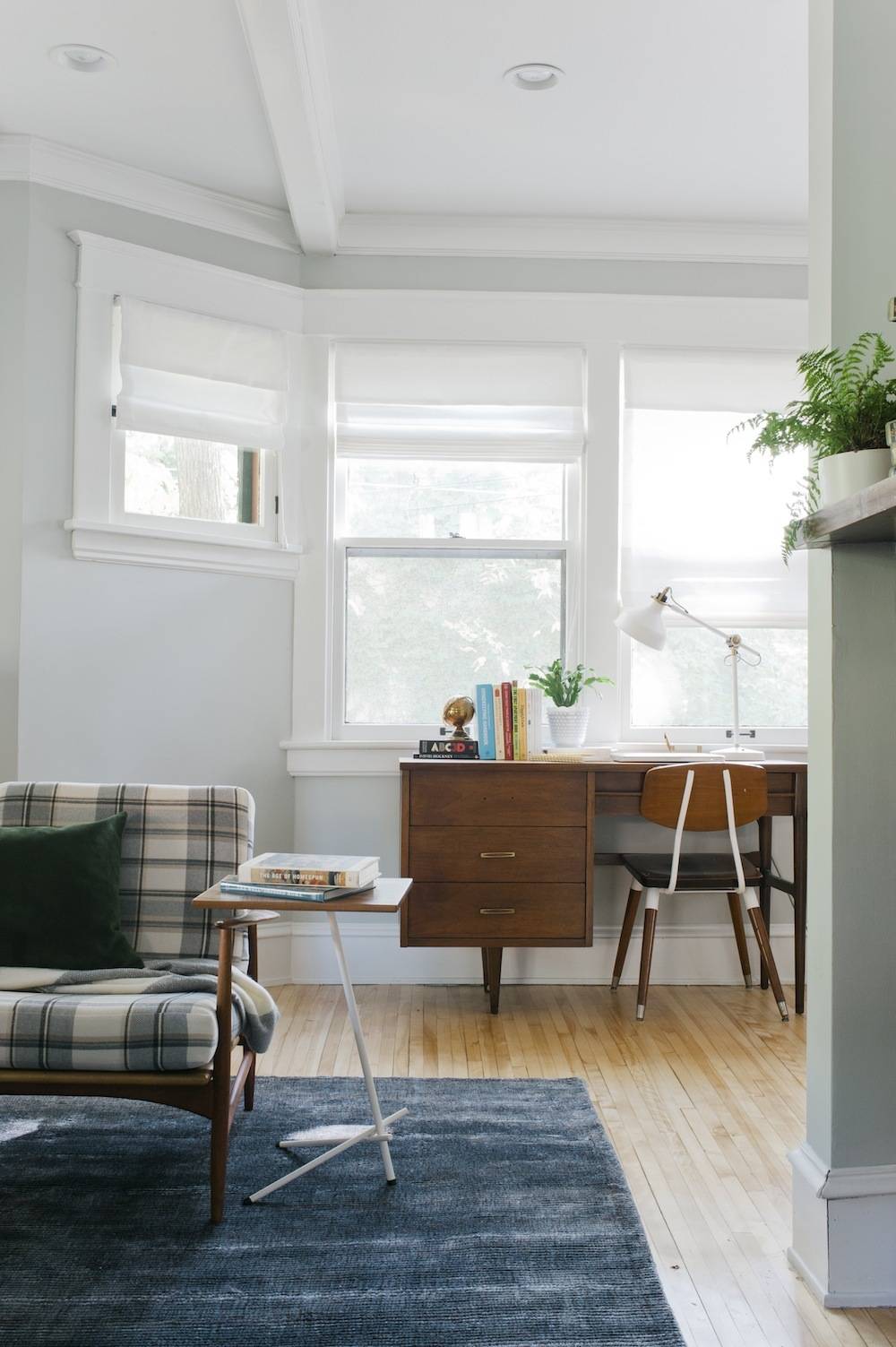 A room having white walls and windows with wooden table and chair situated near the window.