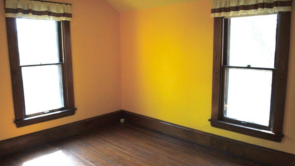 The corner of a yellow room with dark brown window frames and dark brown floors and floor boards.