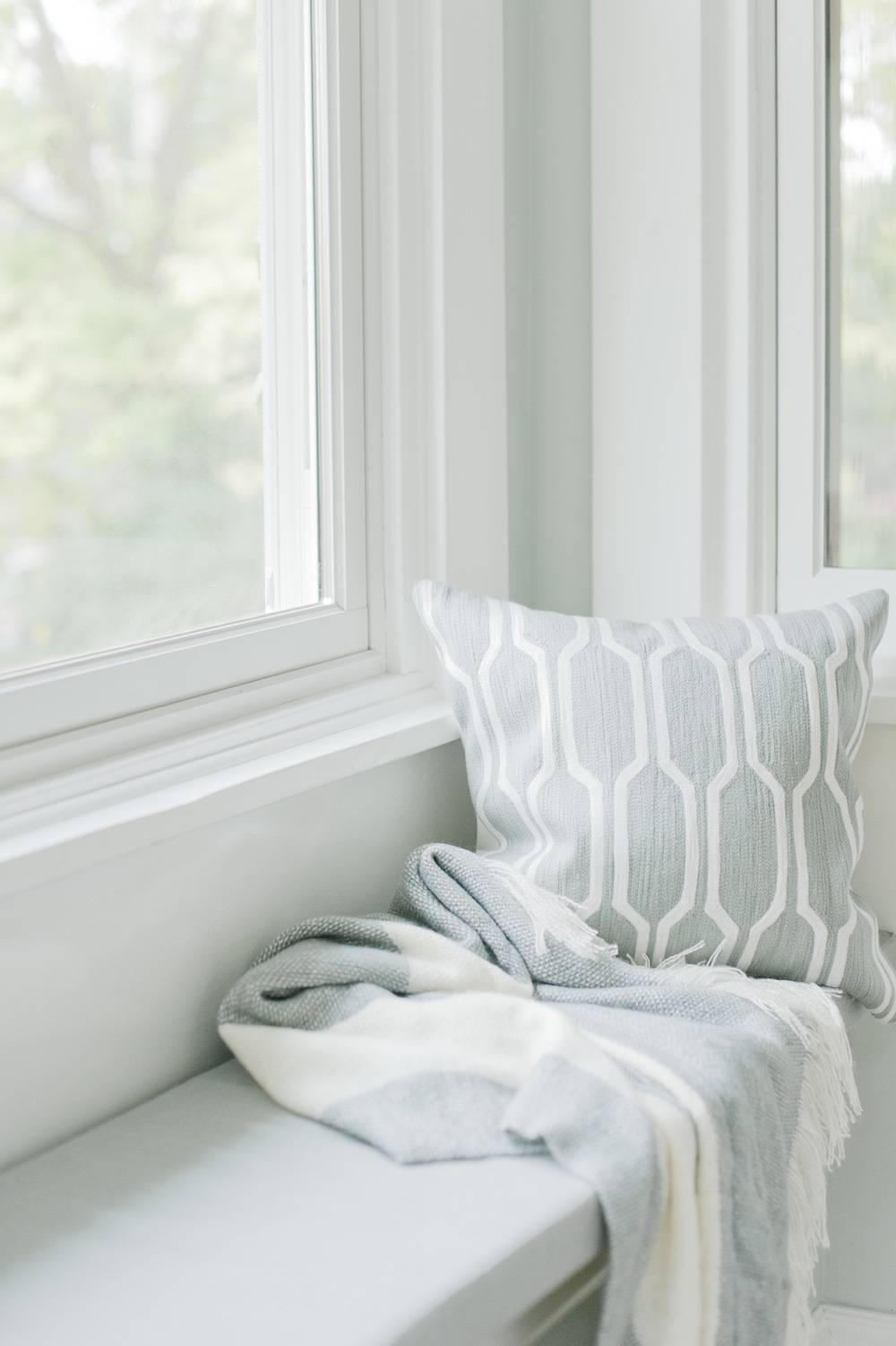A white window seat with a pale gray through and a gray patterned pillow.