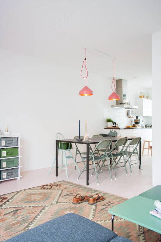 A metal dining table with folding chairs under two orange pendulant lights.