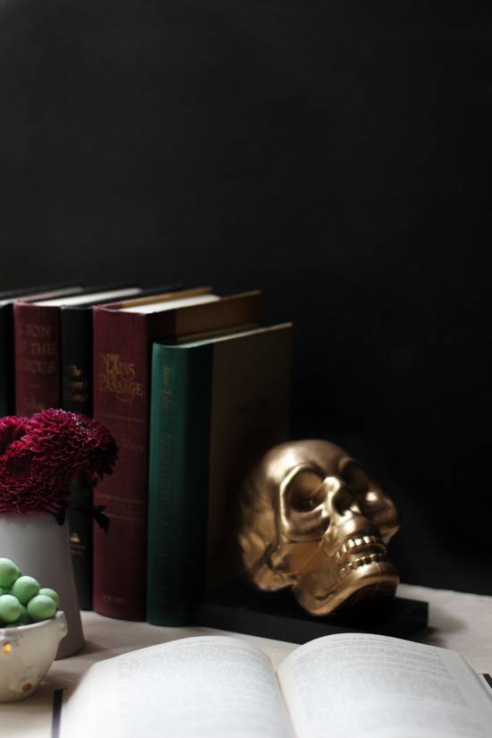 Stack of books with golden skull bookend on table.