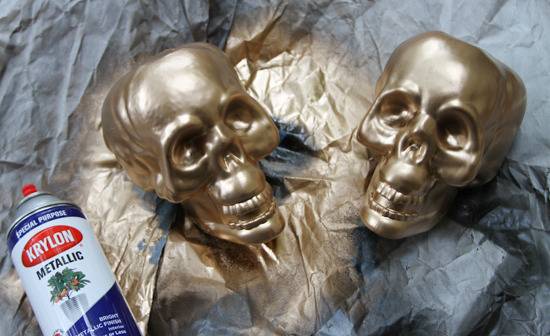 Two skuls spray painted a metallic gold and a metallic spray paint bottle laying next to them.