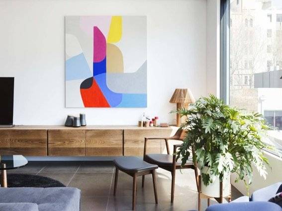 A room has a multi-colored painting plus a potted fern.