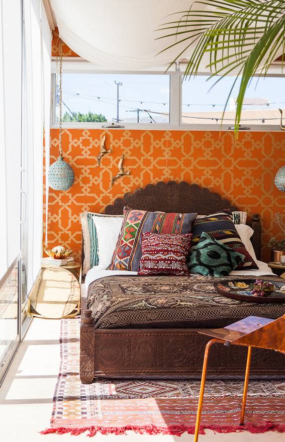 A bedroom has much sunlight and an orange headboard.