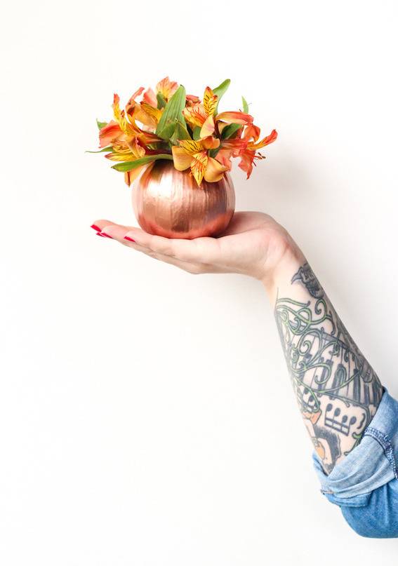 A person with a tattoo on their arm is holding a plant in a gold ball looking pot.