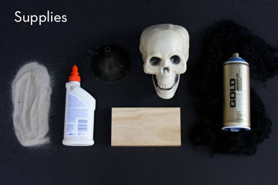 Some white powdery material, a bottle of glue, a skeleton head, a block of wood and a can of gold spray paint.