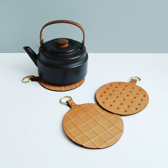A black kettle is next to two brown kitchen hand mats.