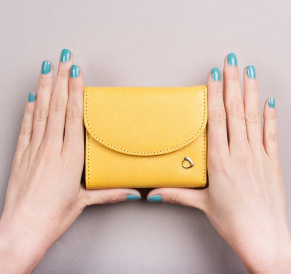 Woman with green nail polish on her nails holding a small yellow hand purse.