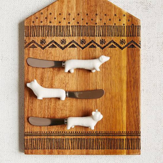 Three butter-knives on a cooking board that are shaped with handles as various dog-breeds.