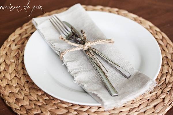 Silverware tied with sisal on linen napkin on plate on top of braided straw mat.
