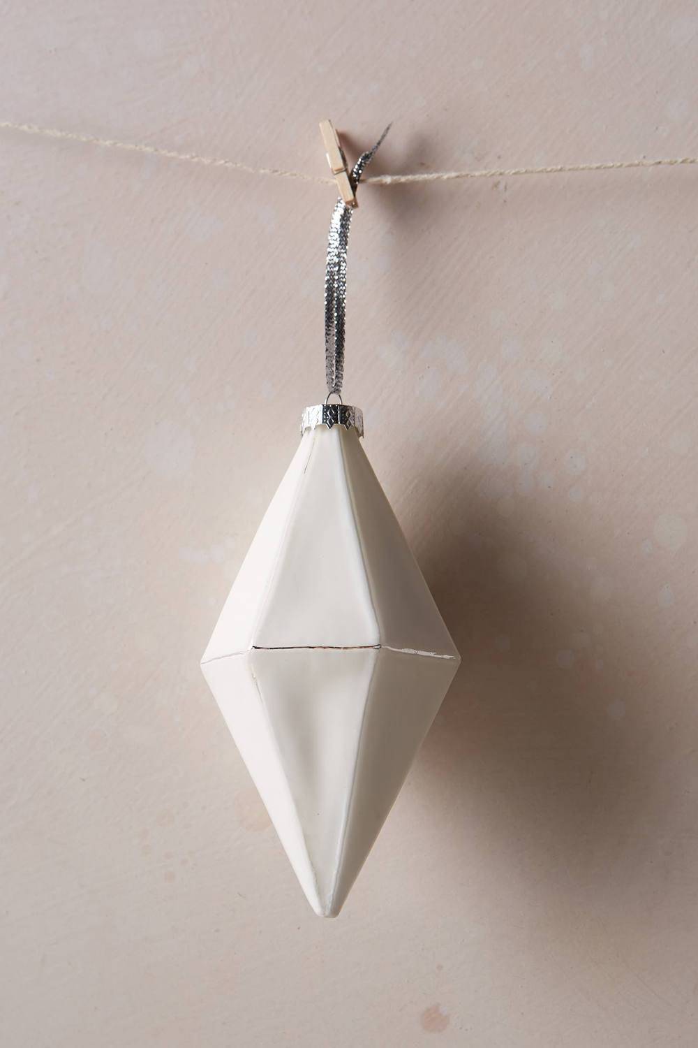 A white diamond ornament hangs on string from a hook on the wall.