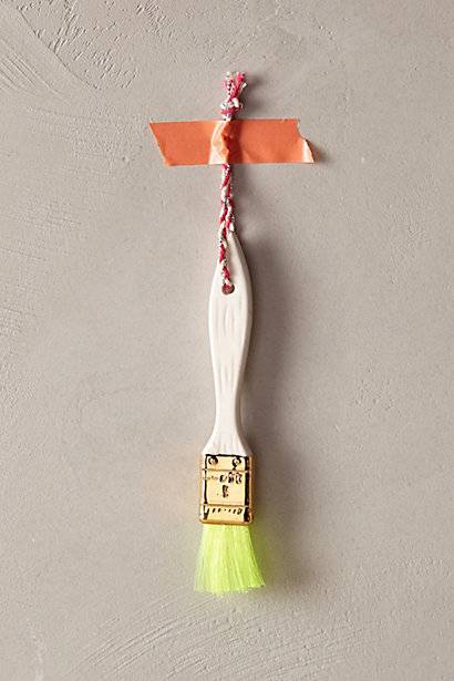 A small lime green brush hangs from a wall by orange tape.