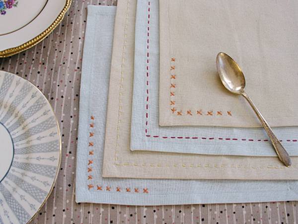A gold spoon sitting on layered grey and tan napkin corners with orange stitching on them.