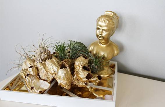 A gold bust up a smiling lady sits on a tray with greenery and other gold bits.