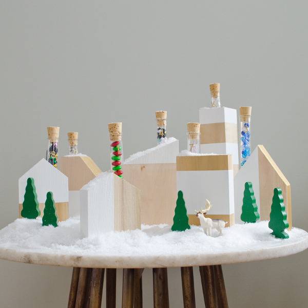 A Christmas village sits on a white disk held up by wooden dowels.
