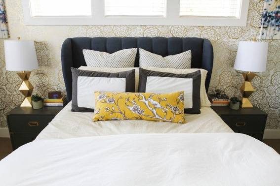 A bed with white sheets and black, white and yellow pillows between two gold lamps.