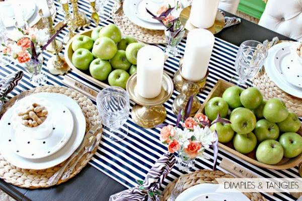 Dinning table with green apples, candles, water glasses, flower vases and plates.