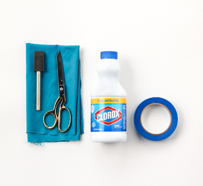 Scissors on top of a blue towel next to a bottle of bleach and blue tape.